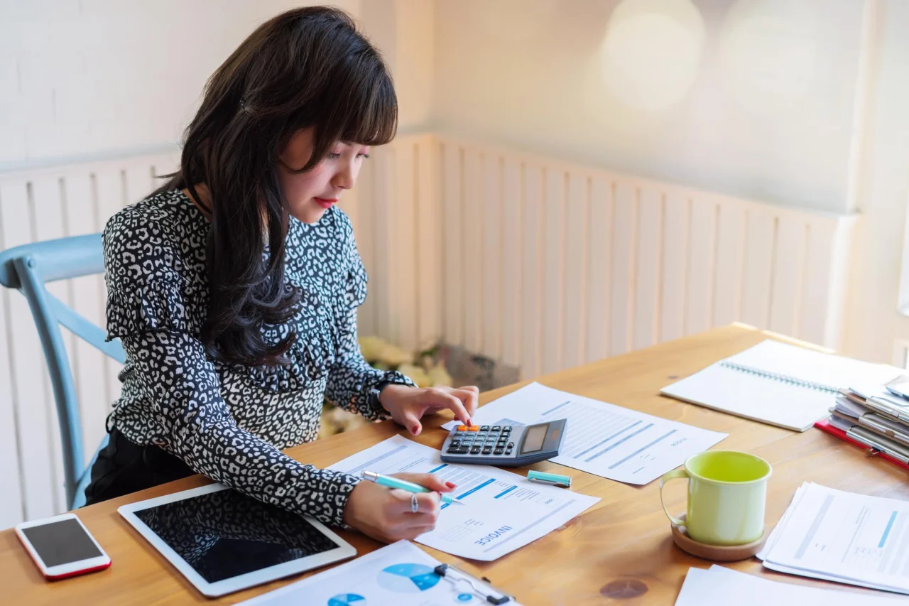A finance professional working through the numbers with a calculator and invoices