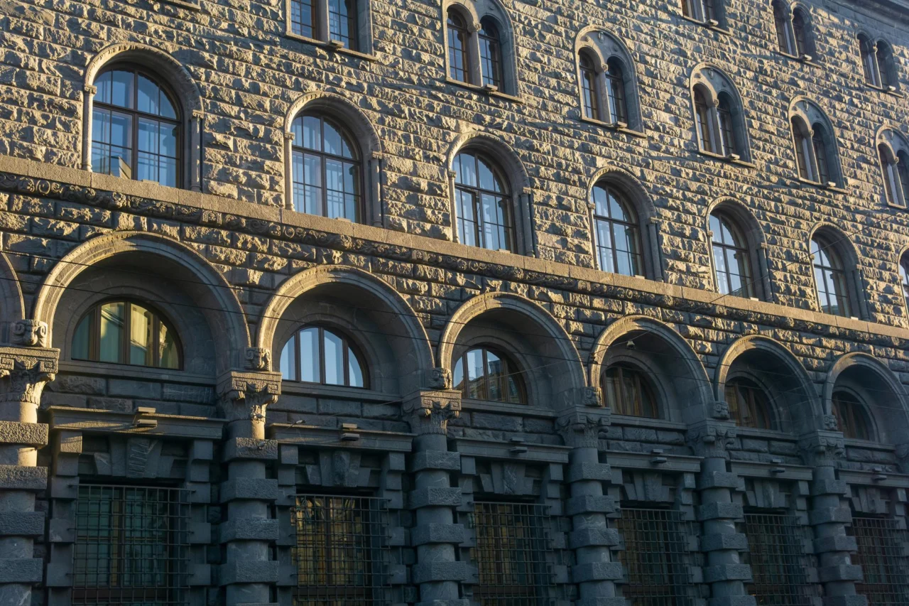 The dark stone facade of an old civic building with arched windows in low morning light