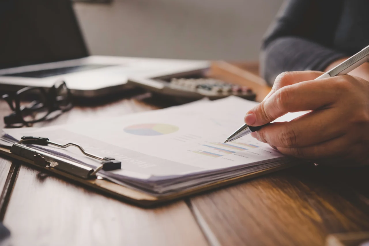 A hand annotating a printed report on a clipboard at a desk
