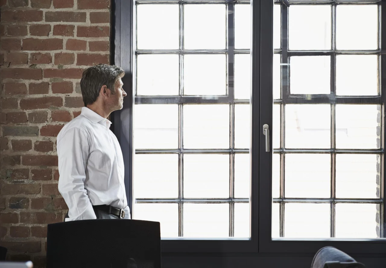 A founder standing alone at a tall office window