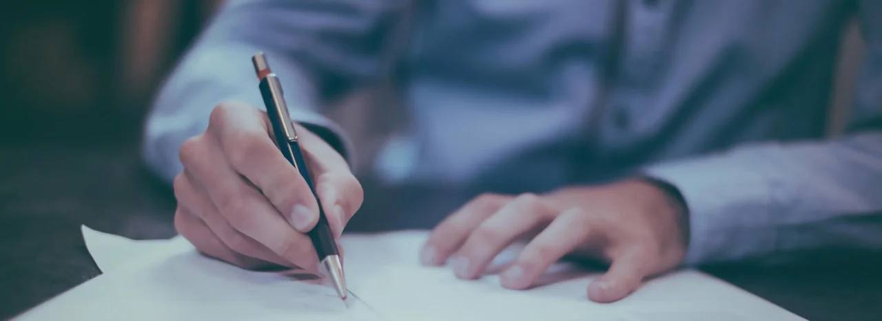 Close-up of a hand signing a document at a desk