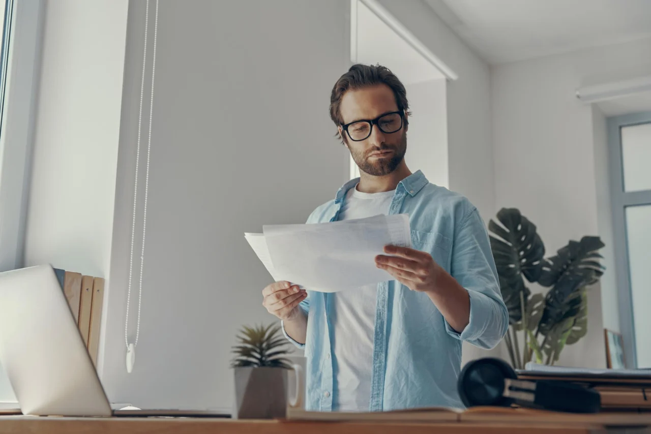 A man standing at his desk reading through a printed document