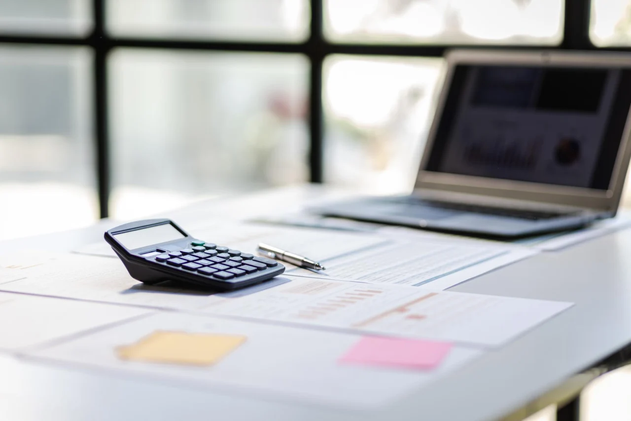 A finance desk with a calculator, financial statements and a laptop