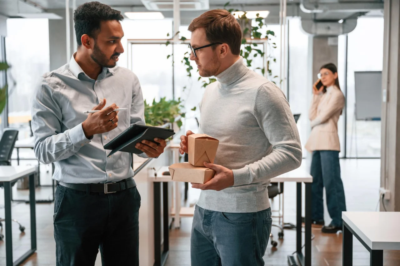 Two colleagues talking in an open-plan office, one holding a tablet