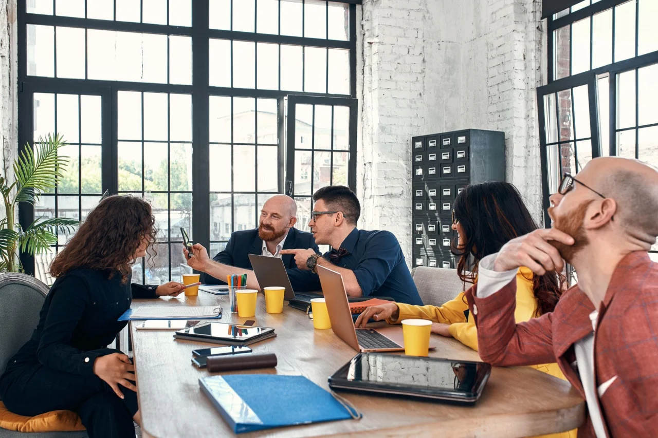 Team of colleagues gathered around a wooden table in a bright loft office discussing documents