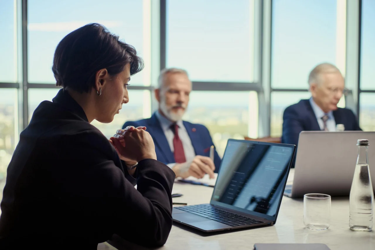 Executive team reviewing laptops during a boardroom meeting with a city skyline in the background