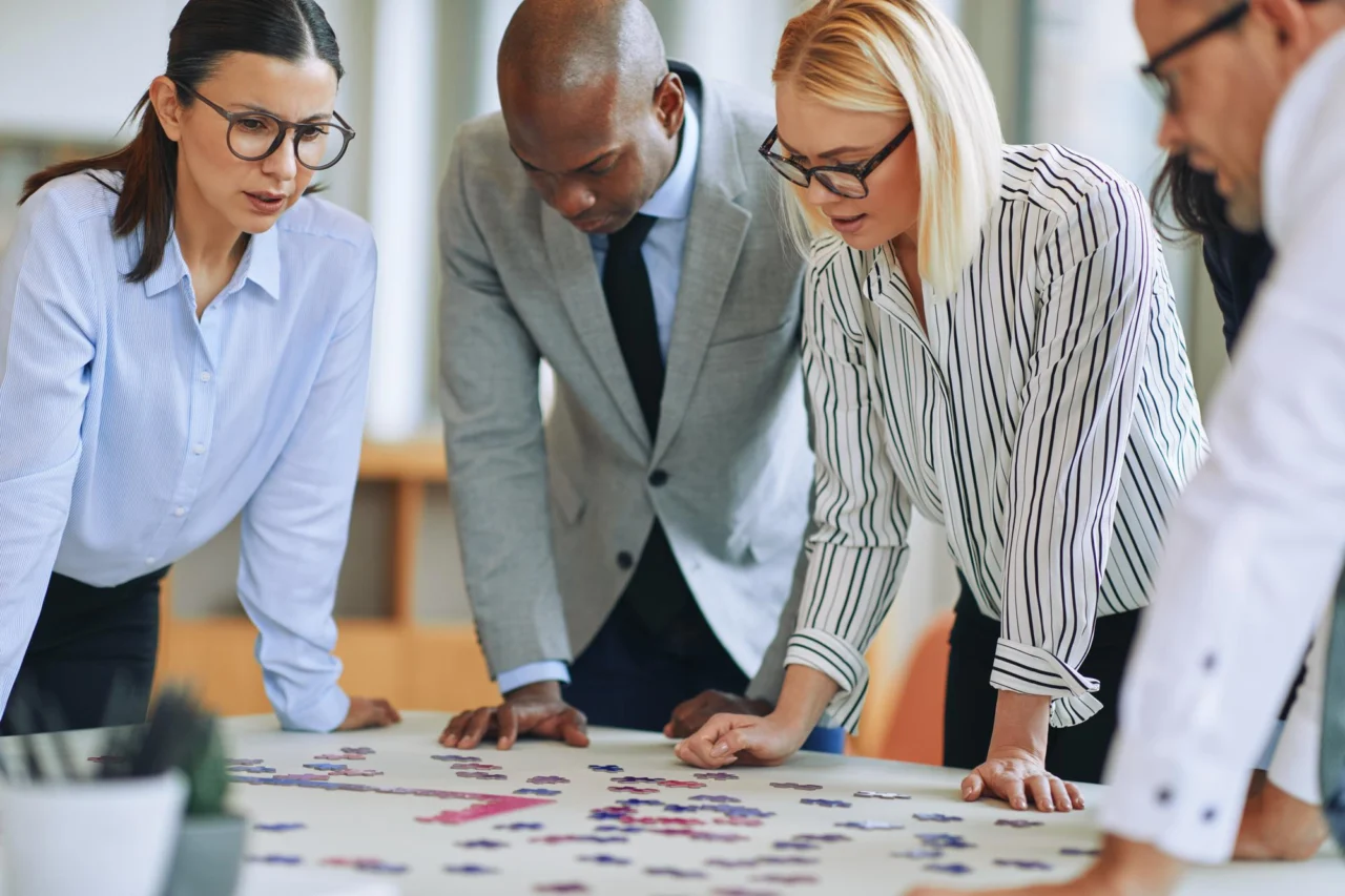 Diverse group of colleagues leaning over a table piecing together a jigsaw puzzle