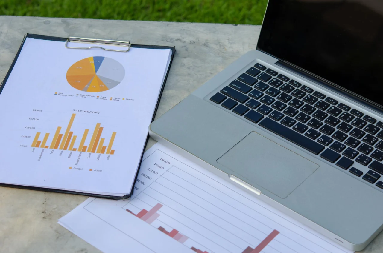 Clipboard with printed bar and pie charts resting beside an open laptop outdoors
