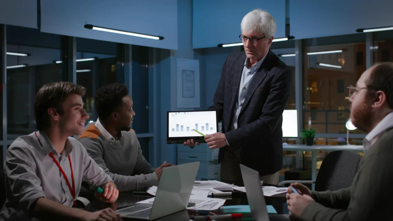 Mature businessman presenting a chart on a tablet to colleagues in a boardroom
