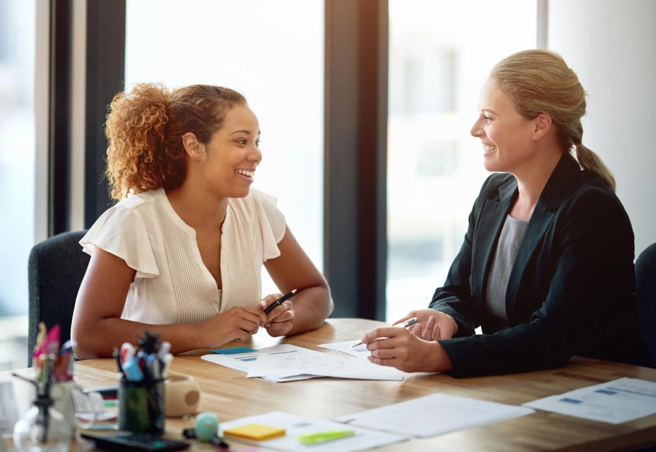 Two businesswomen discussing a contract and agreement paperwork together in an office